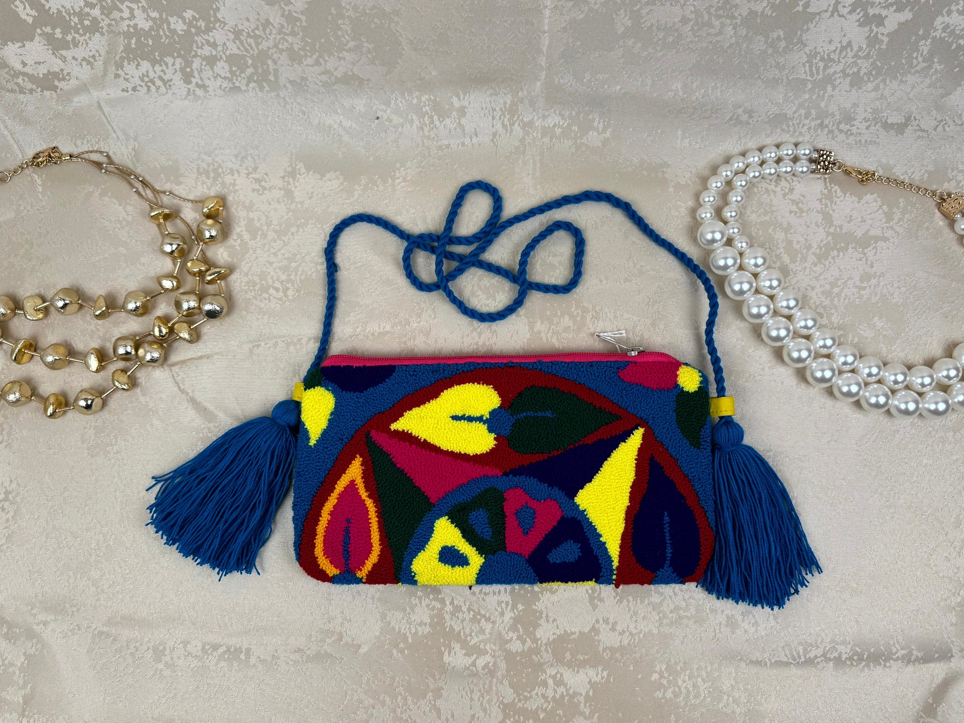 Colorful handbag with tassels on a textured surface with jewelry around