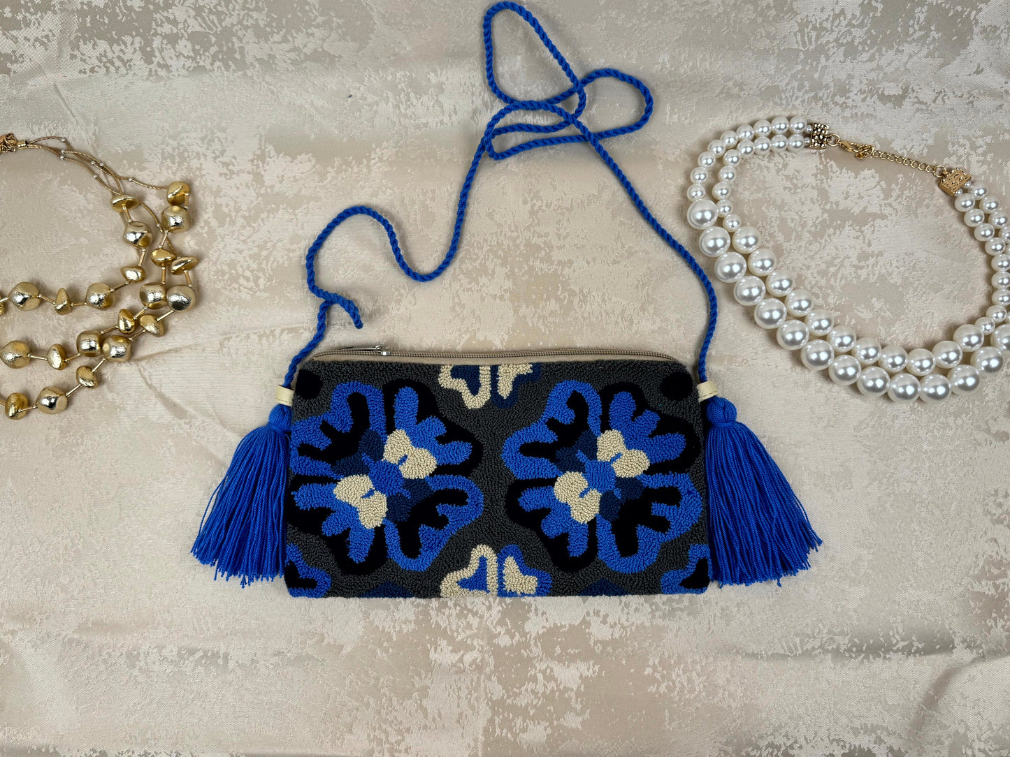 Black clutch with blue floral patterns and tassels on a textured surface