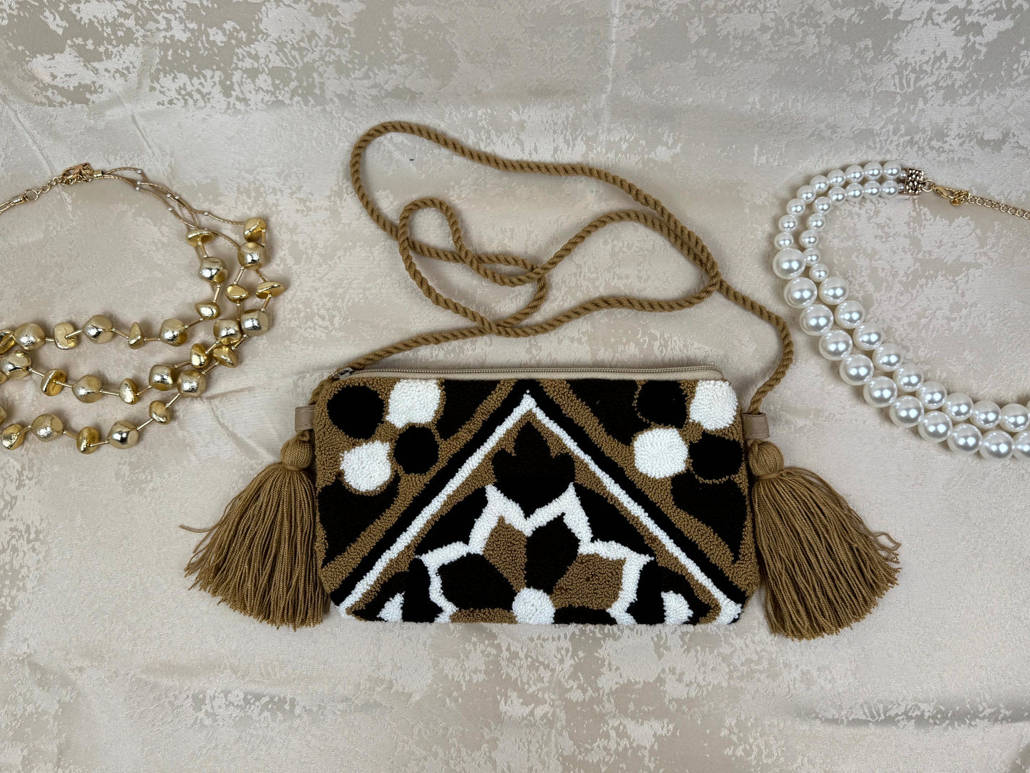Patterned handbag with tassels and two necklaces on a textured surface