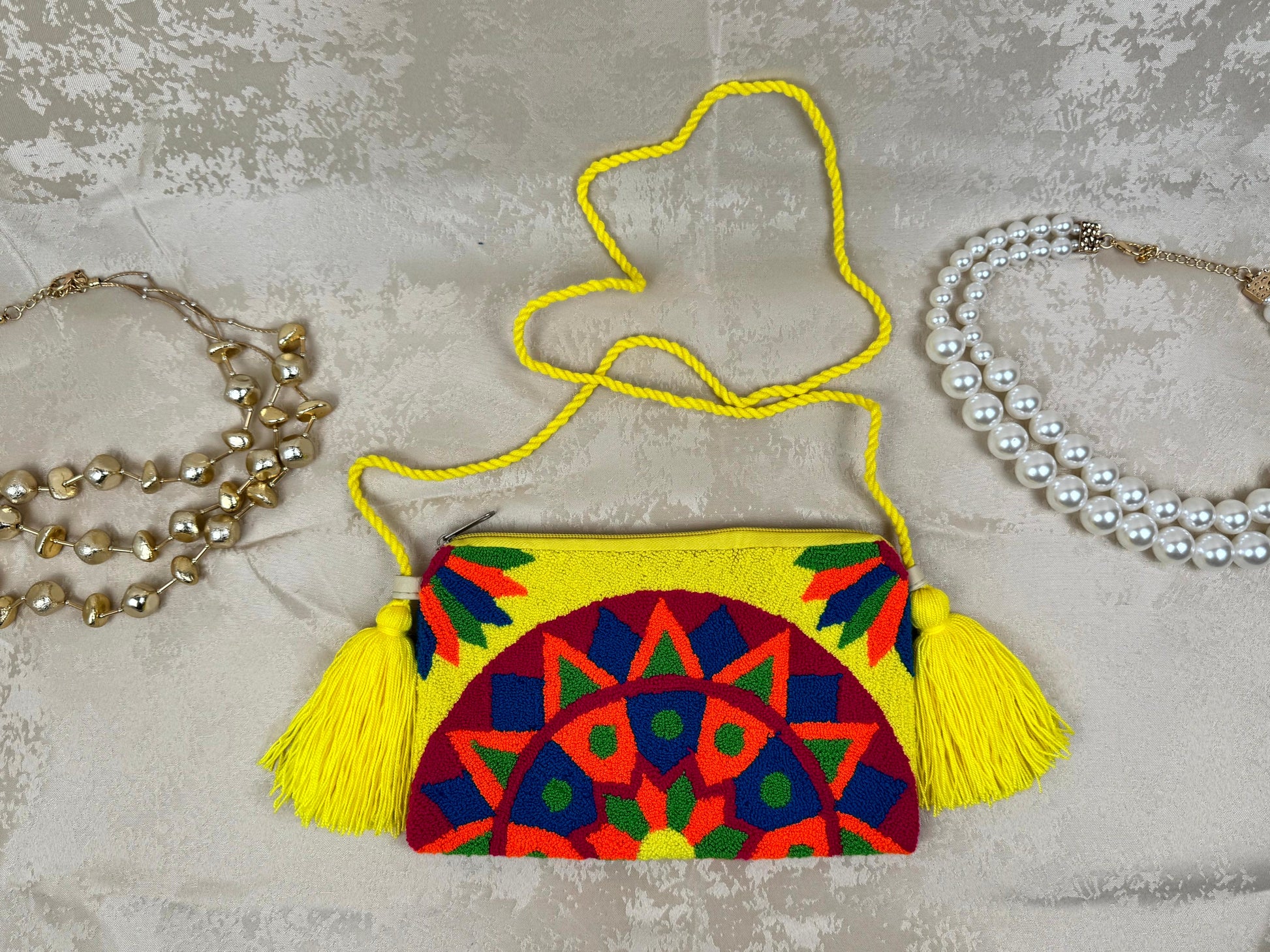 Colorful embroidered handbag with tassels on a textured surface with jewelry.