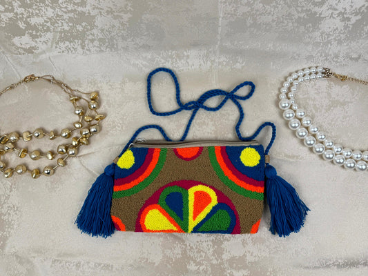 Colorful handbag with geometric design and tassels on a textured surface with jewelry.