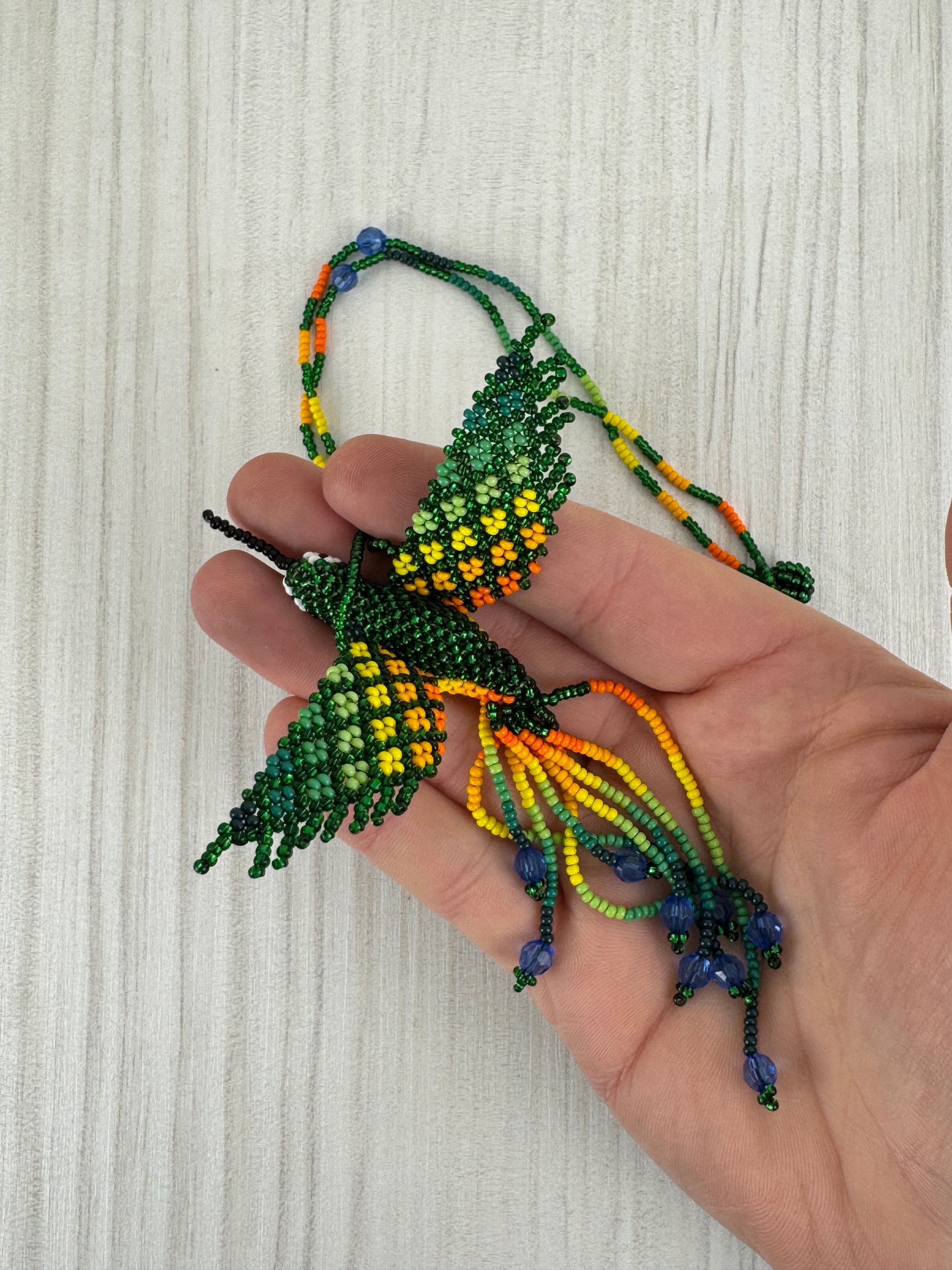 Detalle del pájaro colibri verde tejido a mano en collar artesanal edición limitada.
