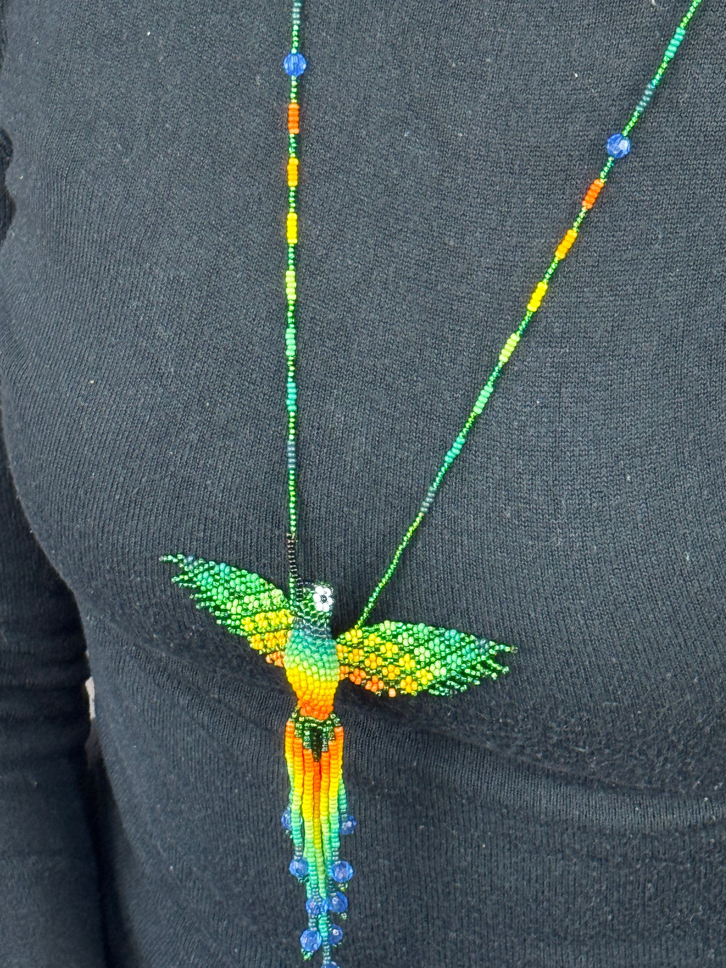 Detalle del tejido artesanal en collar pájaro colibri verde hecho a mano.