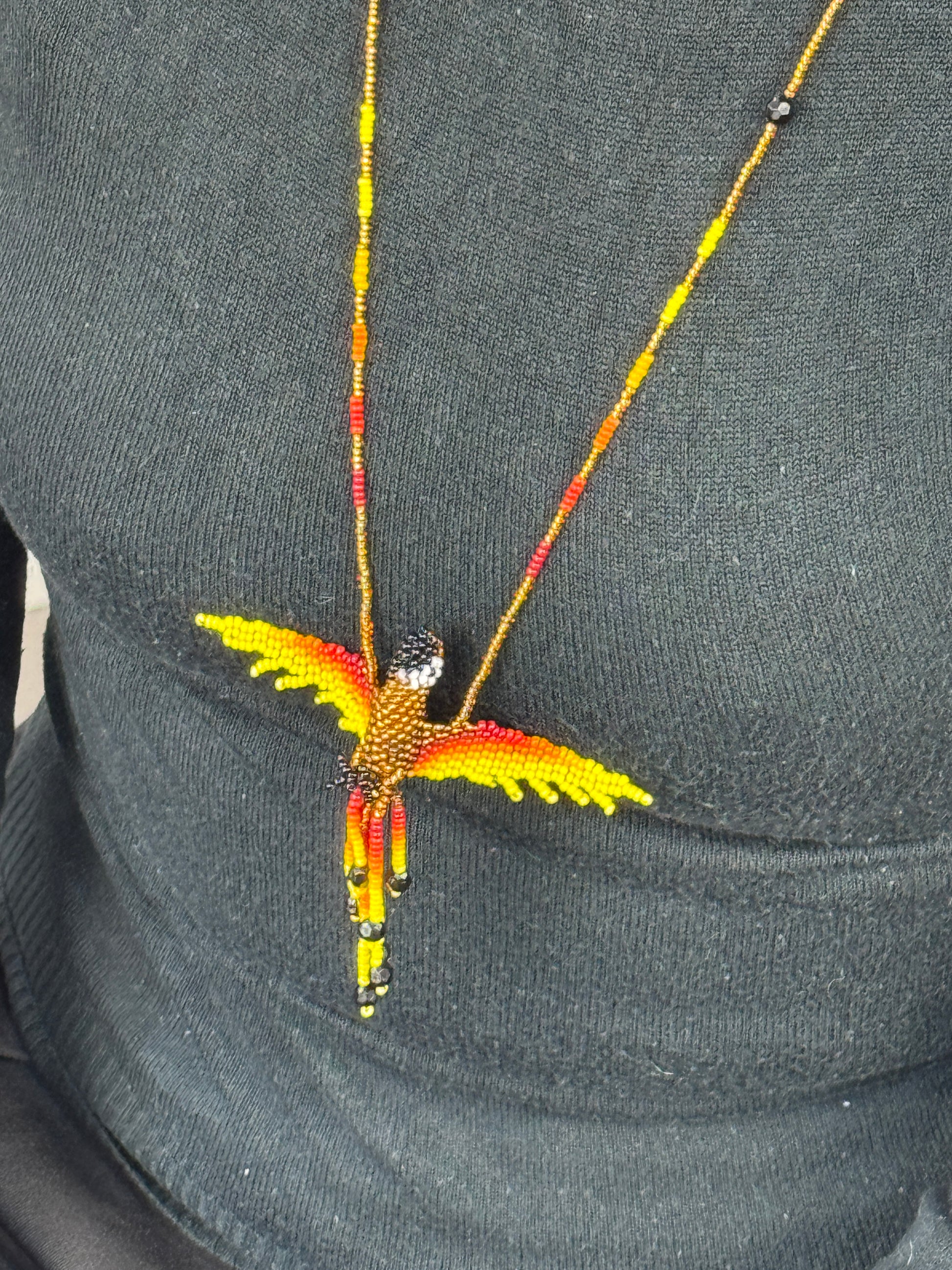 Detalle del tejido artesanal en collar pájaro lloro dorado hecho a mano.