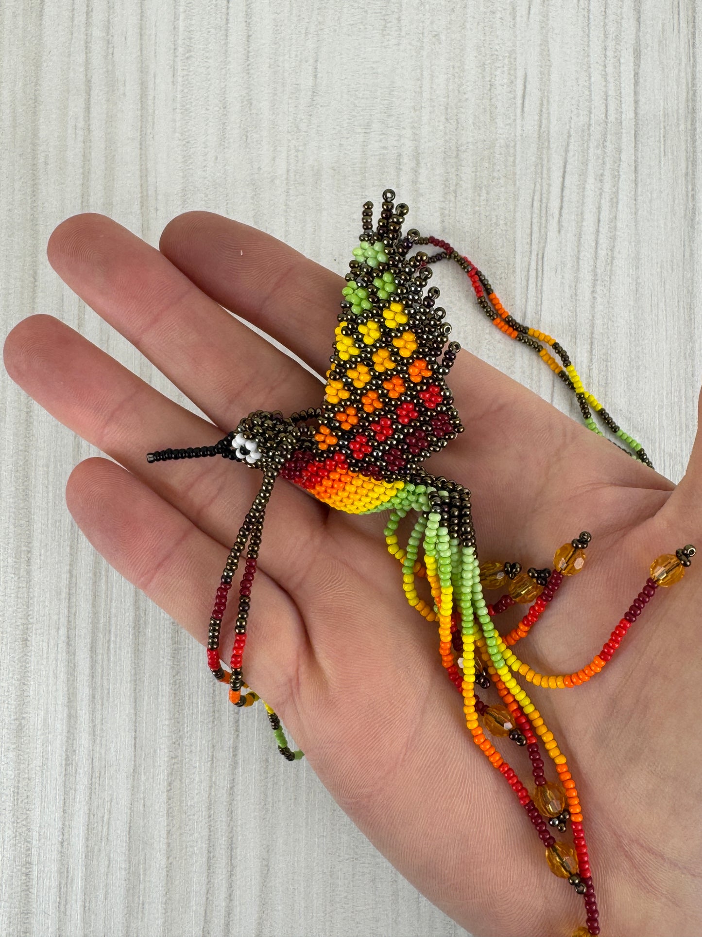 Vista frontal de collar pájaro tejido a mano con diseño artesanal colorido.
