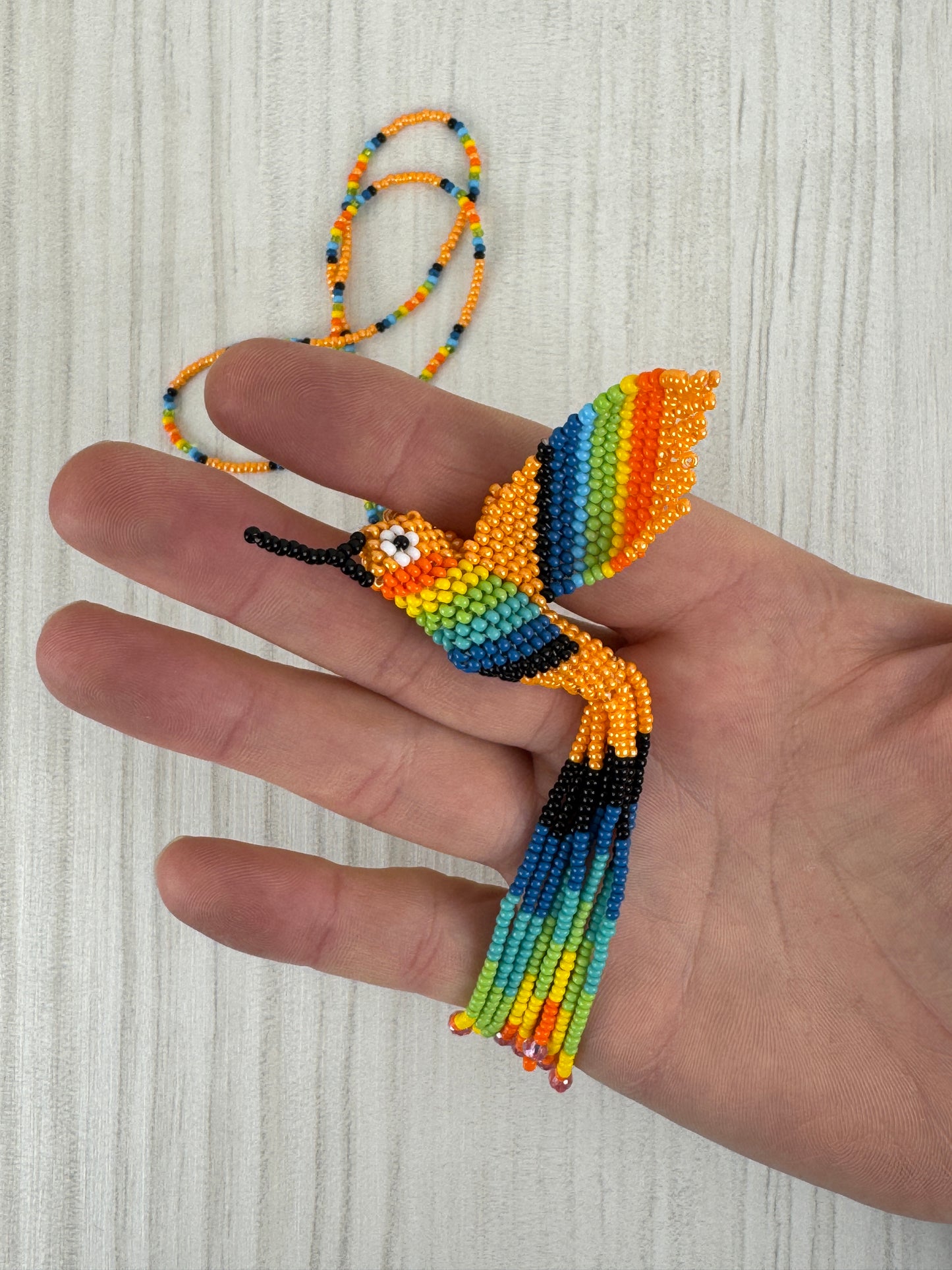 Vista frontal de collar pájaro colibri melocoton tejido a mano con diseño artesanal colorido.