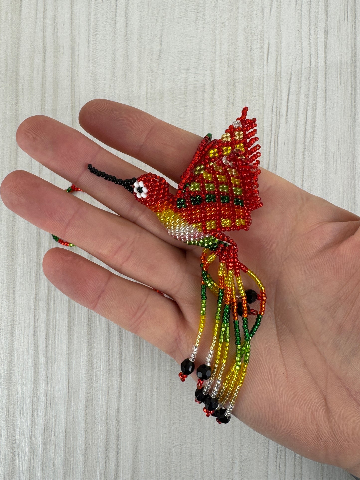 Vista frontal de collar pájaro tejido a mano con diseño artesanal colorido.