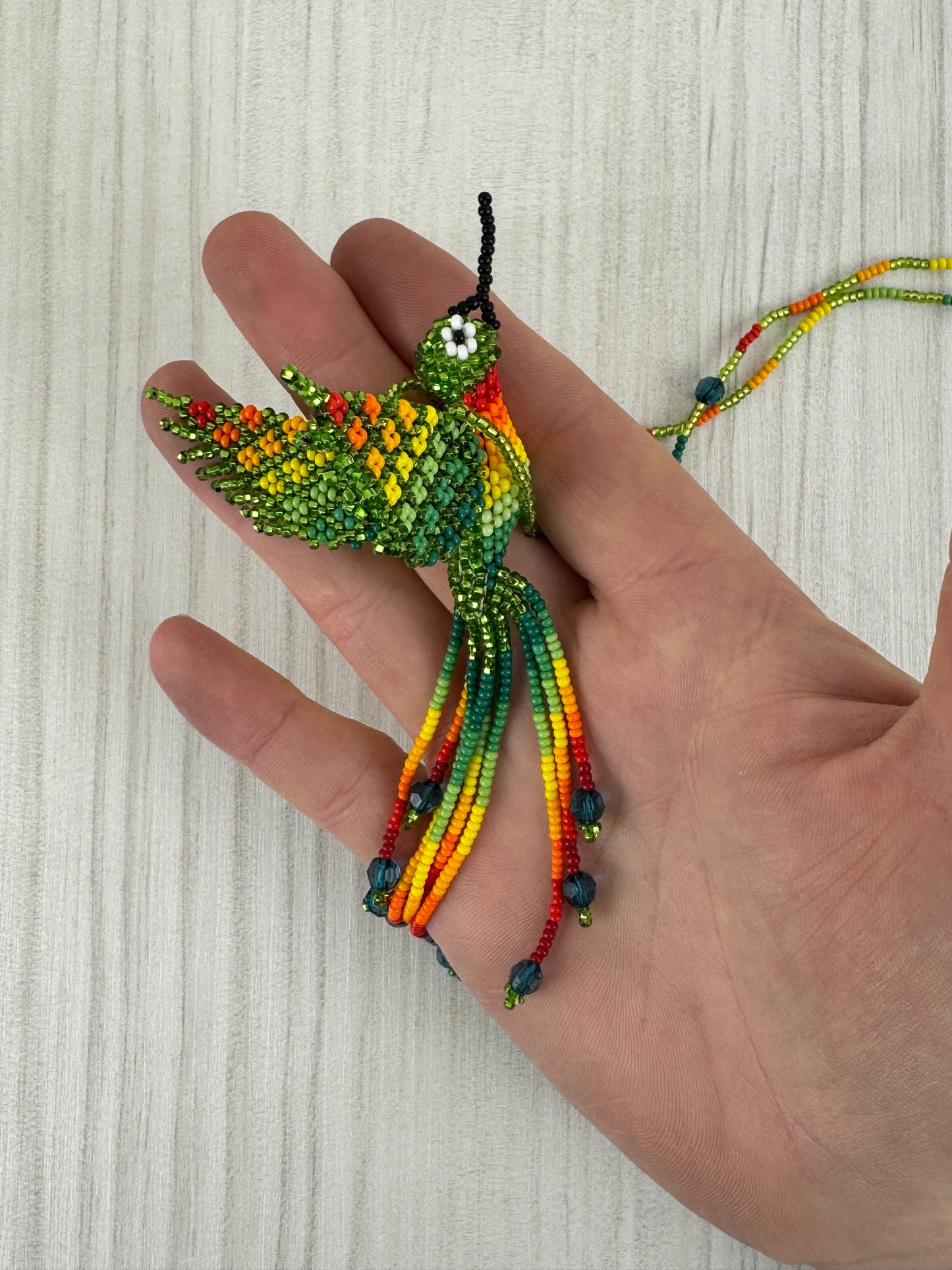 Vista frontal de collar pájaro tejido a mano con diseño artesanal colorido.