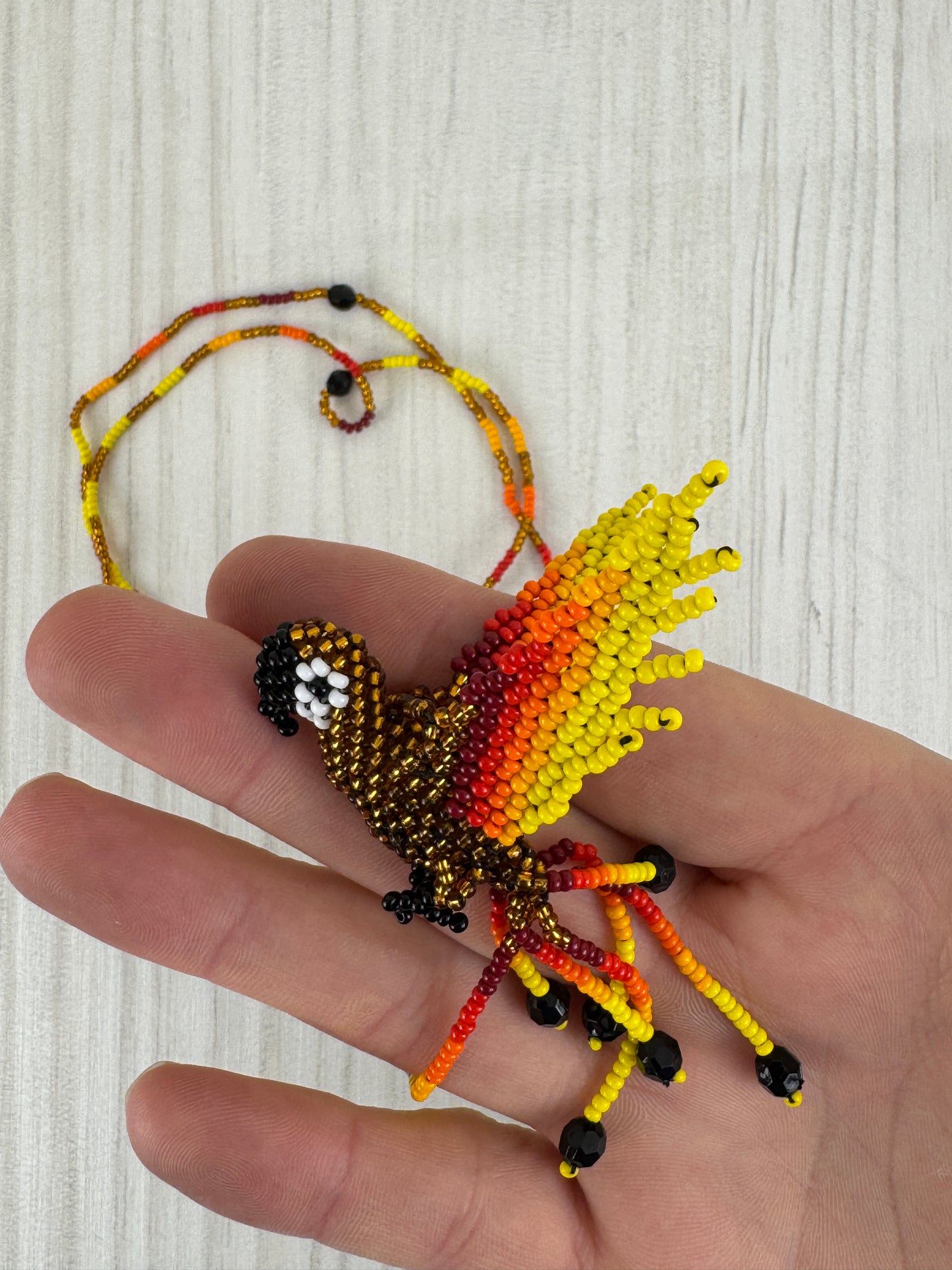 Vista frontal de collar  lloro dorado pájaro tejido a mano con diseño artesanal colorido.