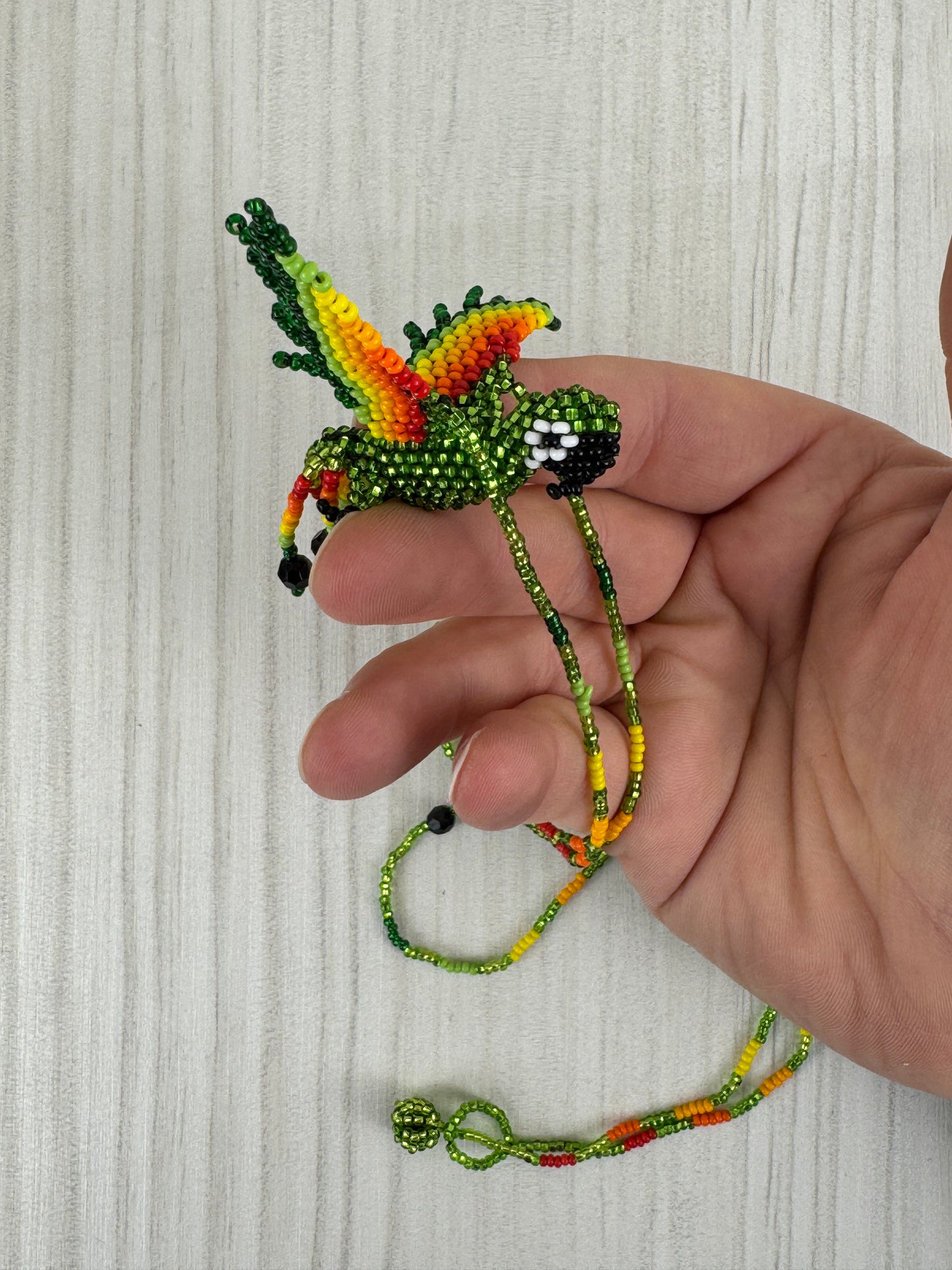 Vista frontal de collar pájaro lloro tejido a mano con diseño artesanal colorido.